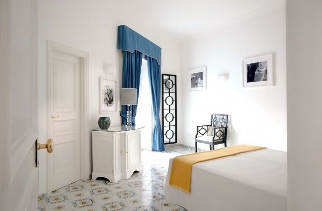 Stanza con tende blu, pavimento decorato e copriletto giallo.