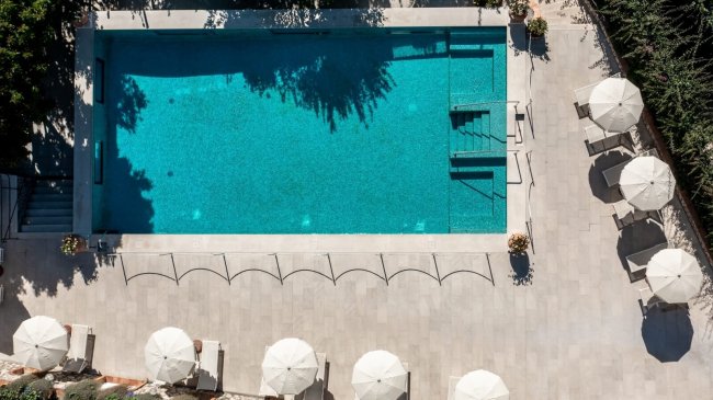 Piscina con ombrelloni e ombre in terrazza.