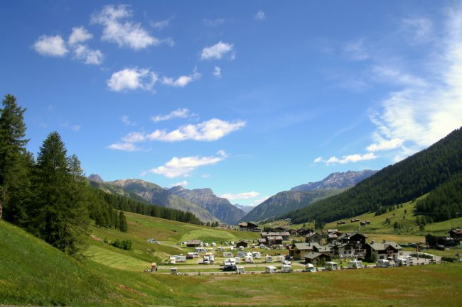 Panorama di montagna con case e camper in una valle verde.