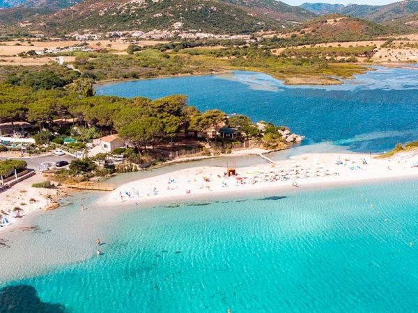 Spiaggia con mare cristallino e colline in lontananza.