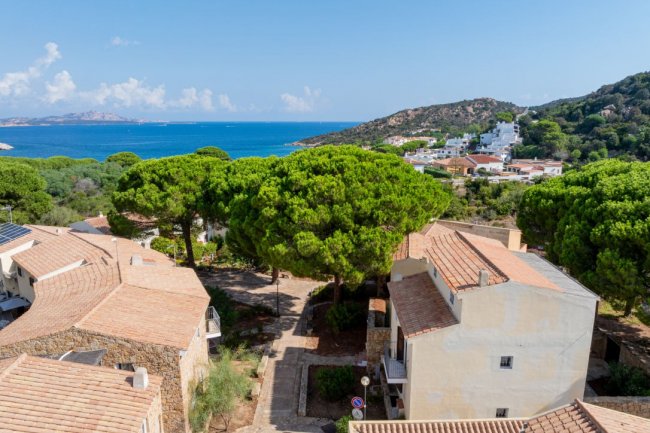 Vista su villette, alberi e mare. Cielo sereno e colline in lontananza.