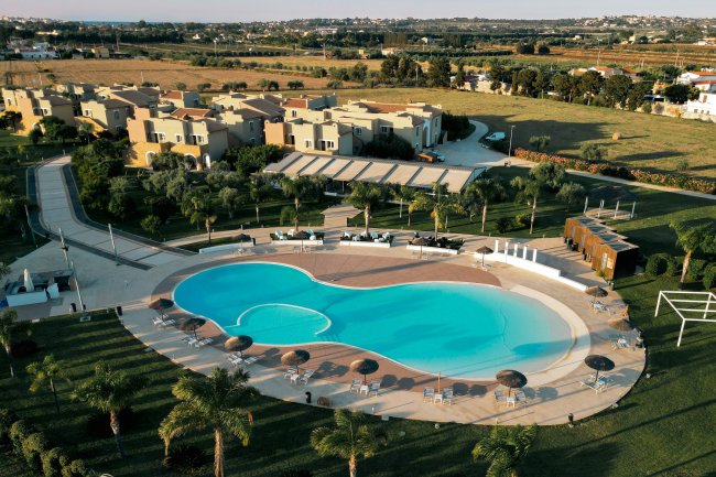 Piscina curvilinea circondata da villette e palme.