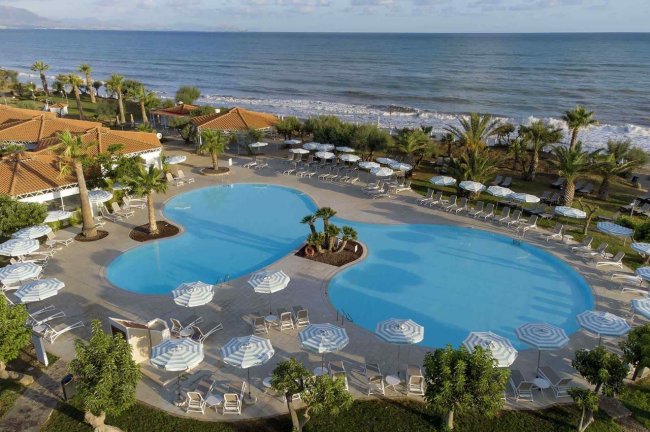 Piscina a forma libera con lettini e ombrelloni vicino al mare.