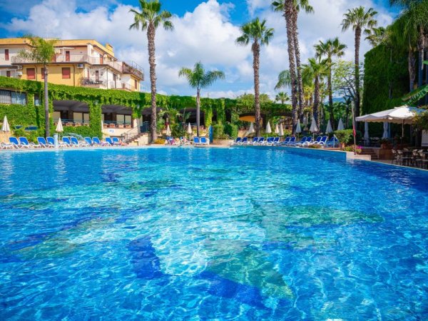 Piscina blu circondata da palme e lettini.