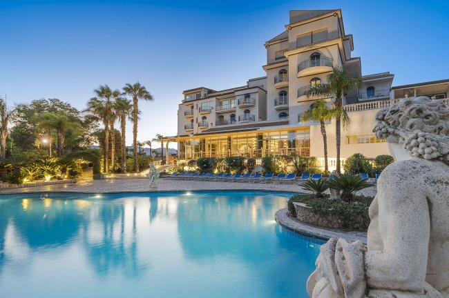 Hotel di lusso con piscina e sculture, al tramonto.