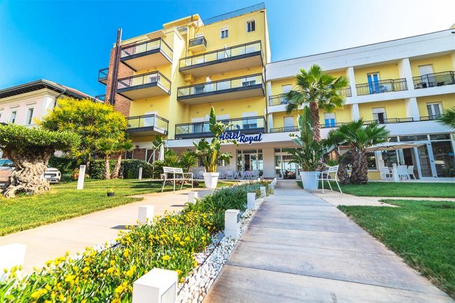 Facciata di un hotel giallo con balconi e giardino.