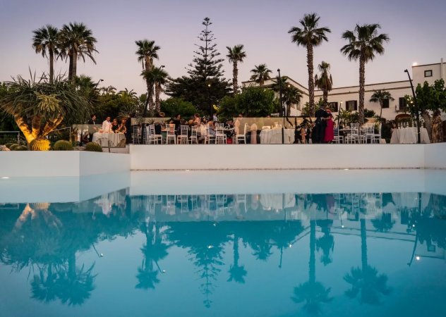 Piscina riflette tavoli allestiti e palme.