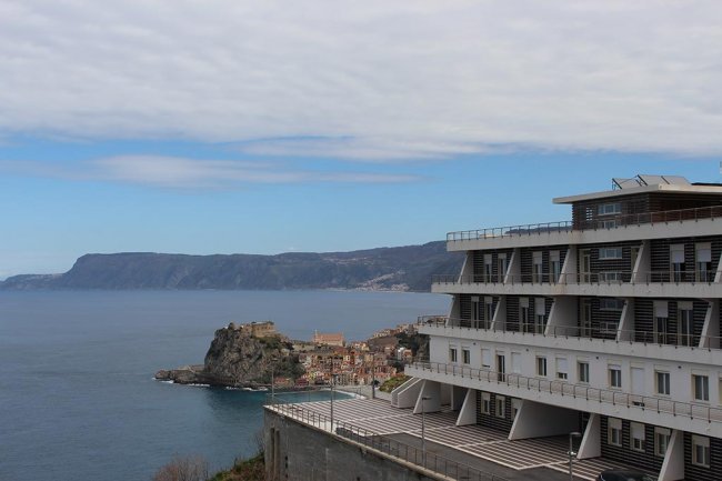 Vista mare con edificio e promontorio in lontananza.