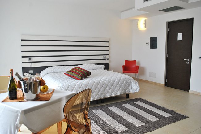 Stanza d'albergo con letto matrimoniale e tavolino con bottiglia.