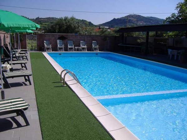 Piscina all'aperto con lettini e ombrelloni verdi.