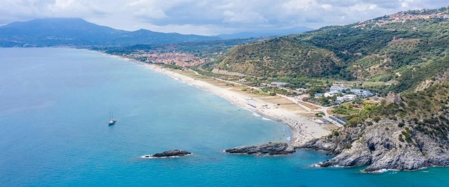 Spiaggia vista dall'alto con mare e montagne.