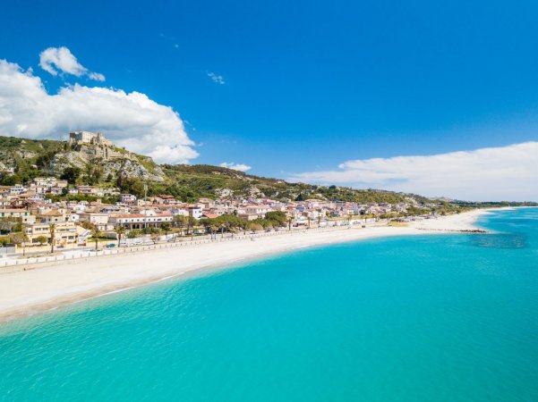 Spiaggia sabbiosa con mare turchese e case sulla costa.