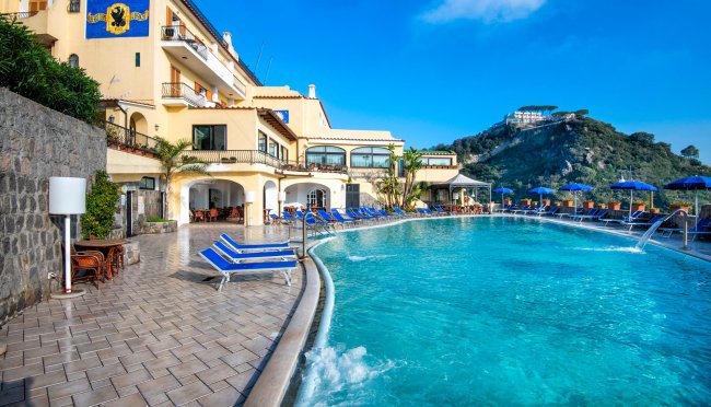 Piscina accanto a un hotel con montagne sullo sfondo.