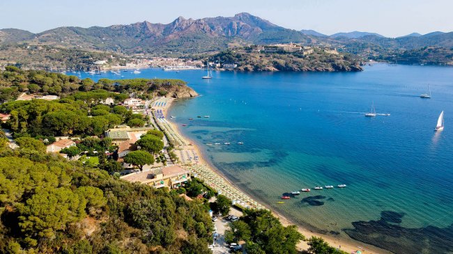 Vista aerea di una spiaggia con barche e montagne.