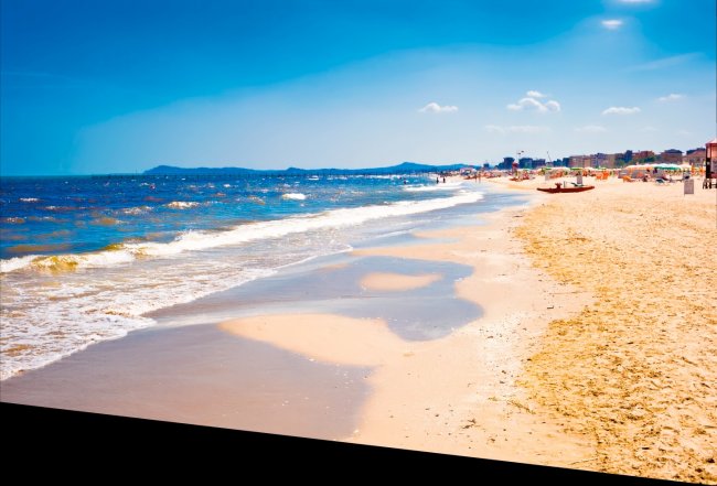 Spiaggia sabbiosa con onde leggere e cielo sereno.