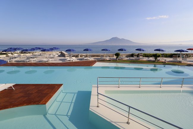 Piscina grande con vista mare e ombrelloni blu.