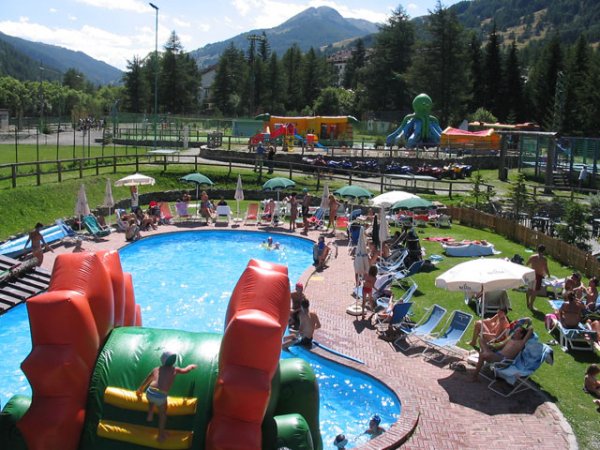 Piscina affollata con ombrelloni e gonfiabile verde.