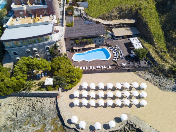 Vista dall'alto di piscina e spiaggia con ombrelloni.