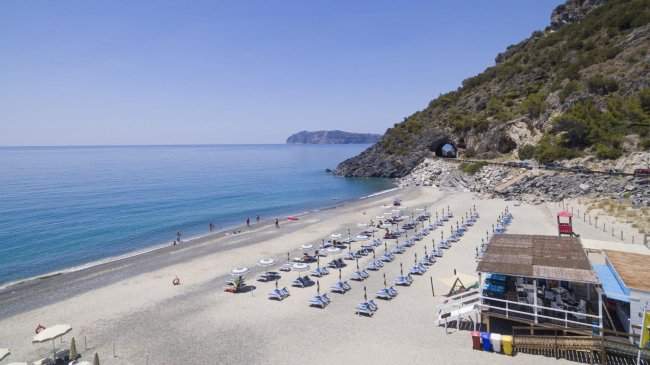 Spiaggia ciottolosa con ombrelloni e lettini vicino a una scogliera.