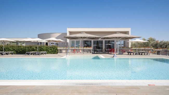 Piscina con ombrelloni e edificio moderno sullo sfondo.