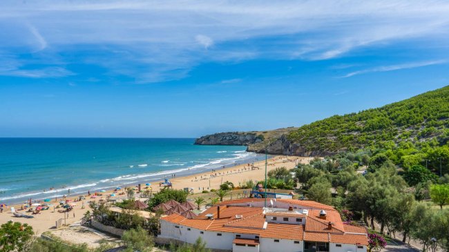 Spiaggia sabbiosa con mare e colline.