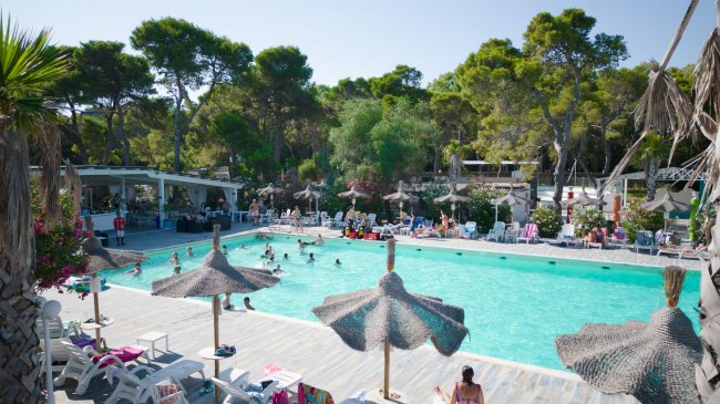 Piscina affollata con ombrelloni di paglia.
