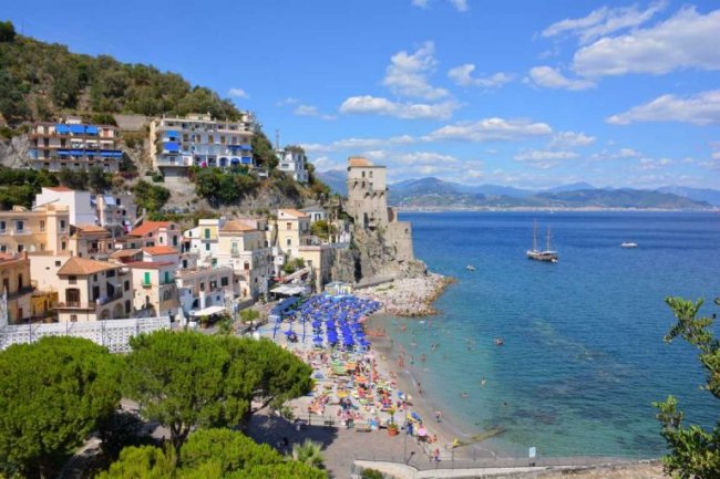 Spiaggia affollata e case colorate sulla costa.