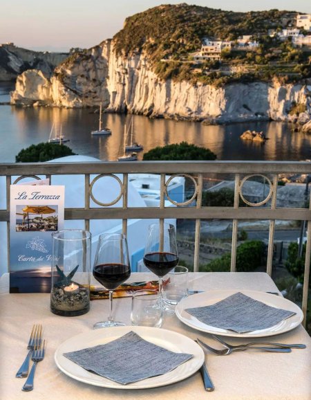 Tavolo apparecchiato su balcone con vista mare.