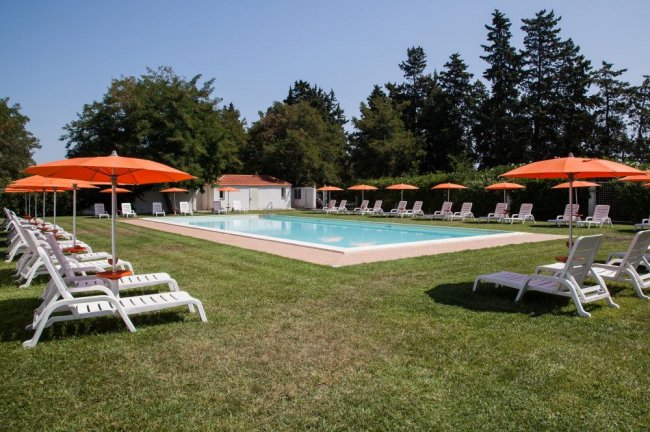 Piscina esterna con lettini bianchi e ombrelloni arancioni.