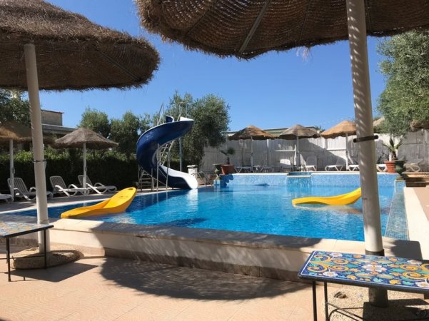 Piscina con scivolo blu e ombrelloni in paglia.