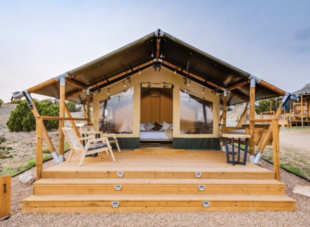 Tenda glamping con veranda in legno e sedie all'esterno.