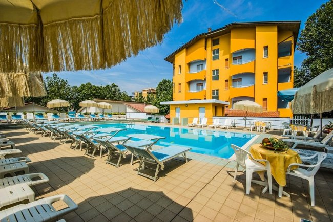 Piscina all'aperto con lettini e edificio giallo sullo sfondo.