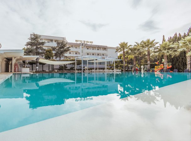 Piscina azzurra riflette l'hotel e palme.