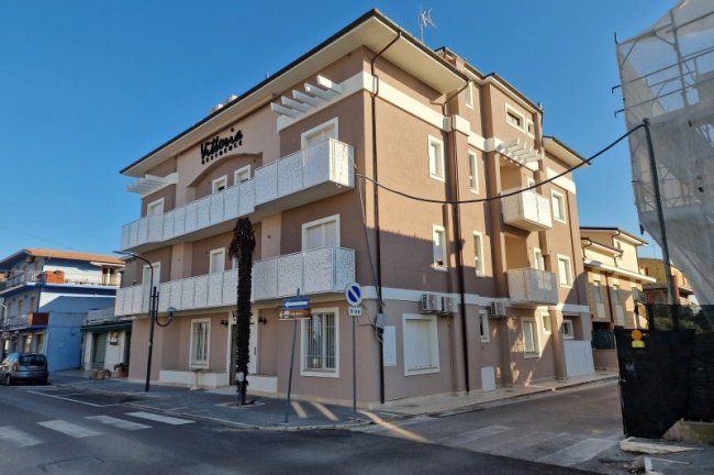 Edificio a più piani, marrone chiaro, con balconi bianchi.