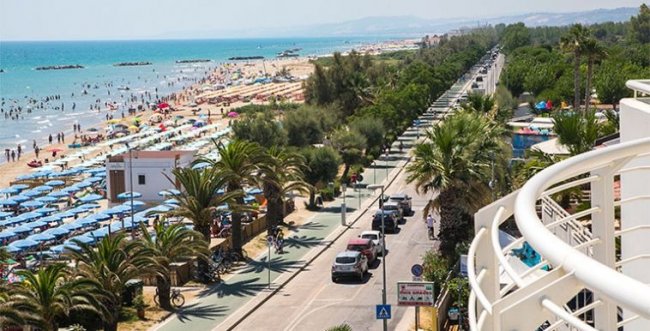 Spiaggia affollata con ombrelloni colorati e strada alberata con auto.