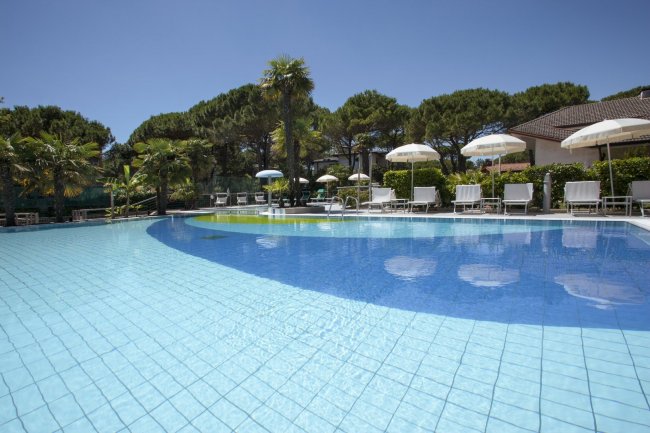 Piscina all'aperto con acqua blu e lettini sotto ombrelloni.