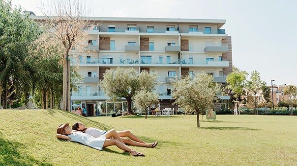 Persone rilassate su prato davanti a edificio.
