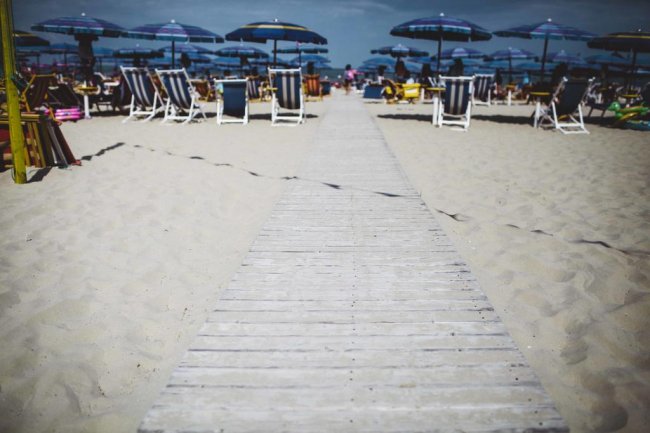 Passerella di legno su una spiaggia con ombrelloni.