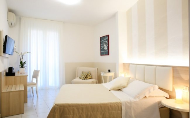 Camera da letto con letto beige, poltrona e TV.