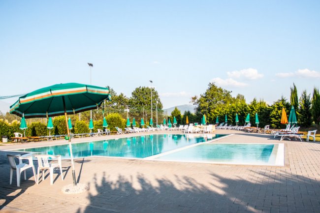 Piscina con ombrelloni verdi e cielo sereno.