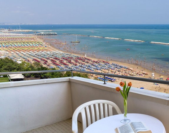Vista spiaggia e mare da un balcone con tavolo e fiori.