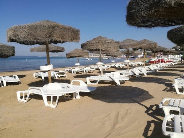 Spiaggia con lettini bianchi e ombrelloni di paglia.