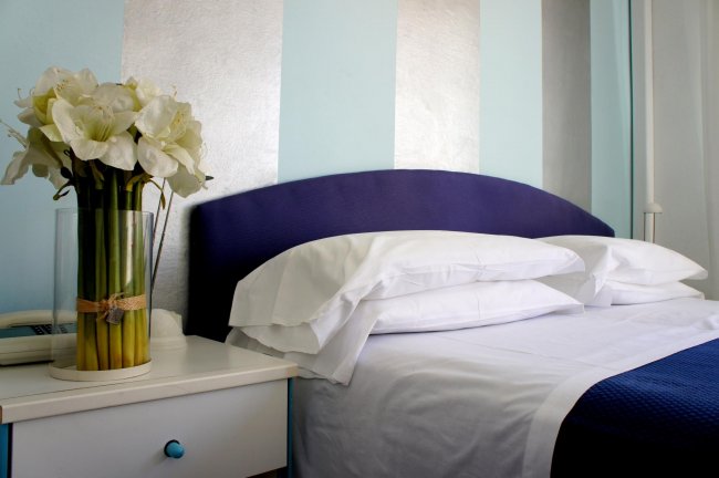 Camera da letto con pareti azzurre e un vaso di fiori bianchi sul comodino.