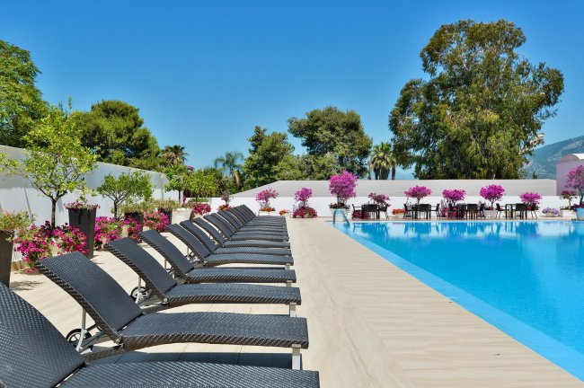 Lettini accanto a una piscina con fiori e alberi sullo sfondo.