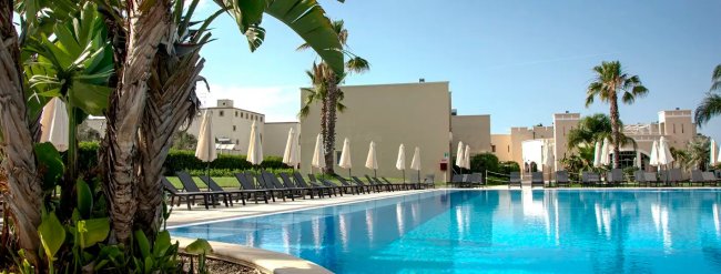 Piscina con lettini, ombrelloni e palme.