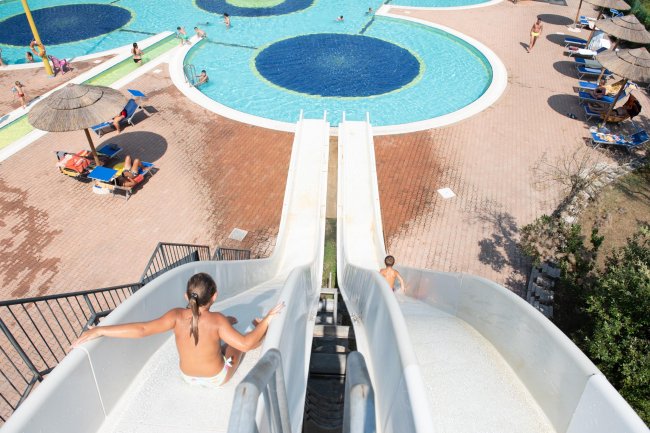 Persone scivolano su due acquascivoli verso una piscina.