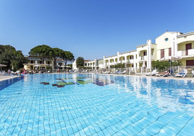 Ampia piscina con lettini, edifici bianchi attorno.