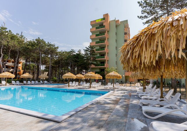 Piscina circondata da alberi e ombrelloni di paglia.