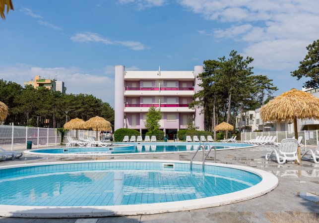 Una piscina circondata da sedie a sdraio e ombrelloni di paglia.