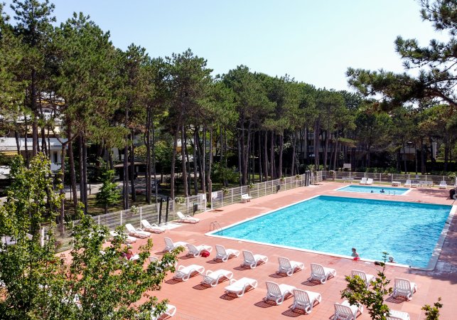 Piscina all'aperto circondata da sedie a sdraio e alberi.